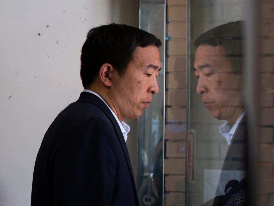 Andrew Yang walks past his reflection in a window.