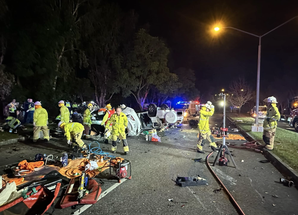 Paramedics and emergency rescue workers at the two-car crash scene in Brisbane on Saturday night. Debris can be seen strewn across the road. 