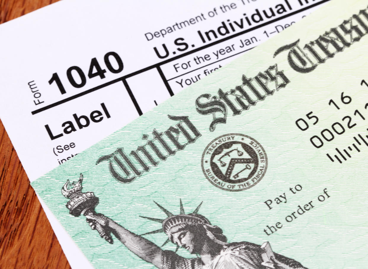 Partial view of a USA tax refund check showing the Treasury seal and image of the Statue of Liberty. Check is on top of an IRS form 1040 tax return. Shot against a wood desk background. 