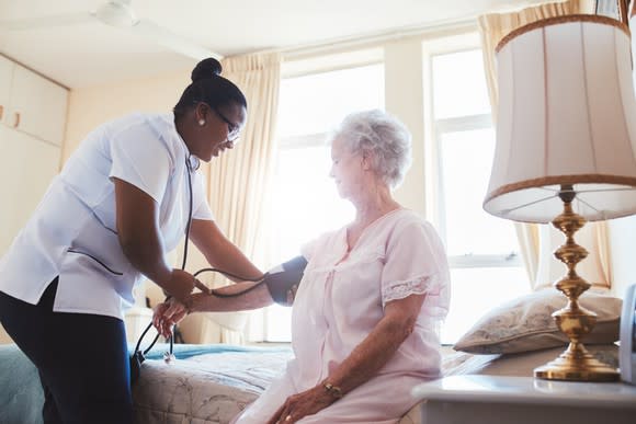 Older woman in a hospital bed having her blood pressure checked.