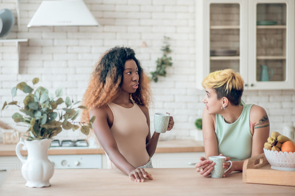 Two people drinking coffee and talking in a kitchen