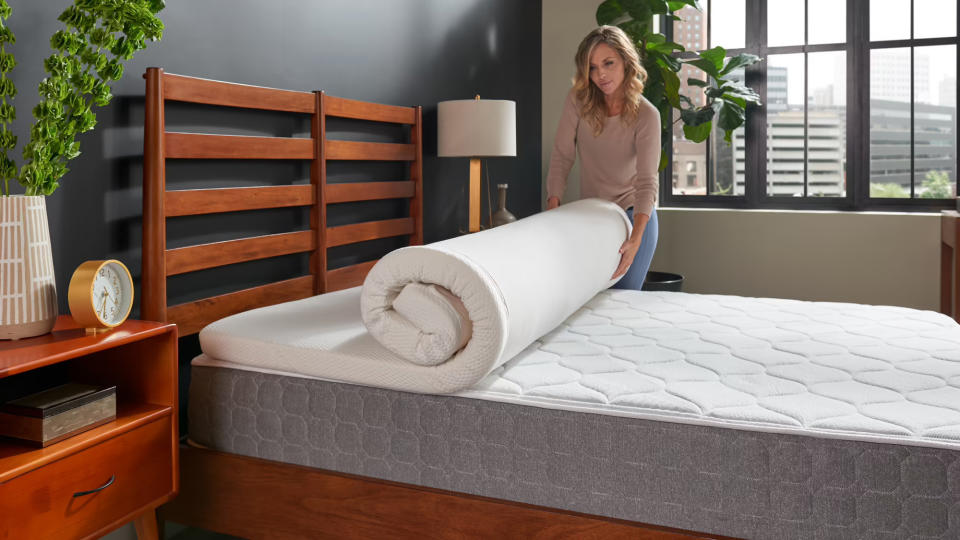 A woman unrolls the Tempur Topper Supreme on her wooden bed frame