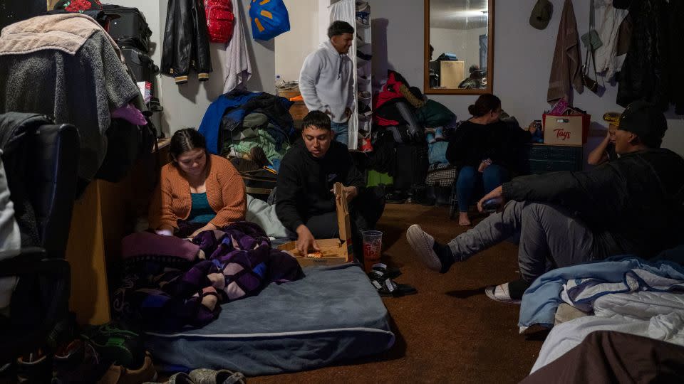 A group of people camp out in one of the rooms at Yong Prince’s motel. Carlo, center, eating pizza, said Prince had been like a mother to the migrants, cooking them breakfast every day before they went to look for work. - Evelio Contreras/CNN