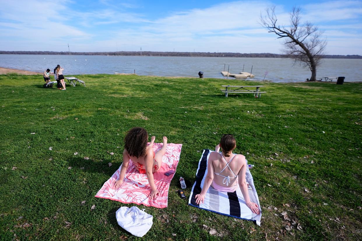 Natalie Dean, left, and Katlyn Butler enjoy an unseasonably warm winter day on the shore of Joe Pool Lake, Monday, Feb. 26, 2024, in Grand Prairie, Texas. Dozens of locations across the central U.S. set record high temperatures on Monday.