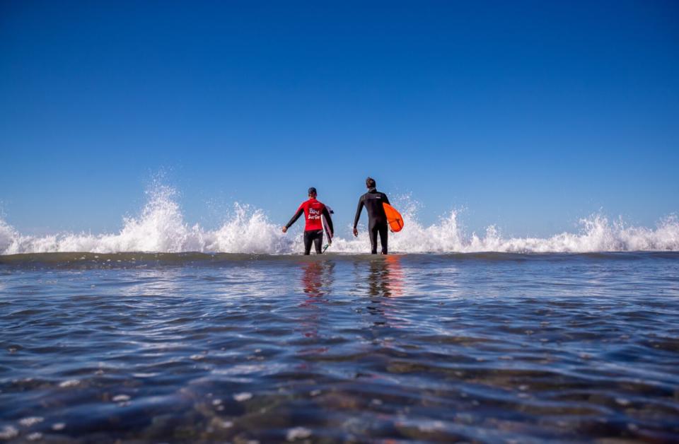 Two men walk into the ocean.