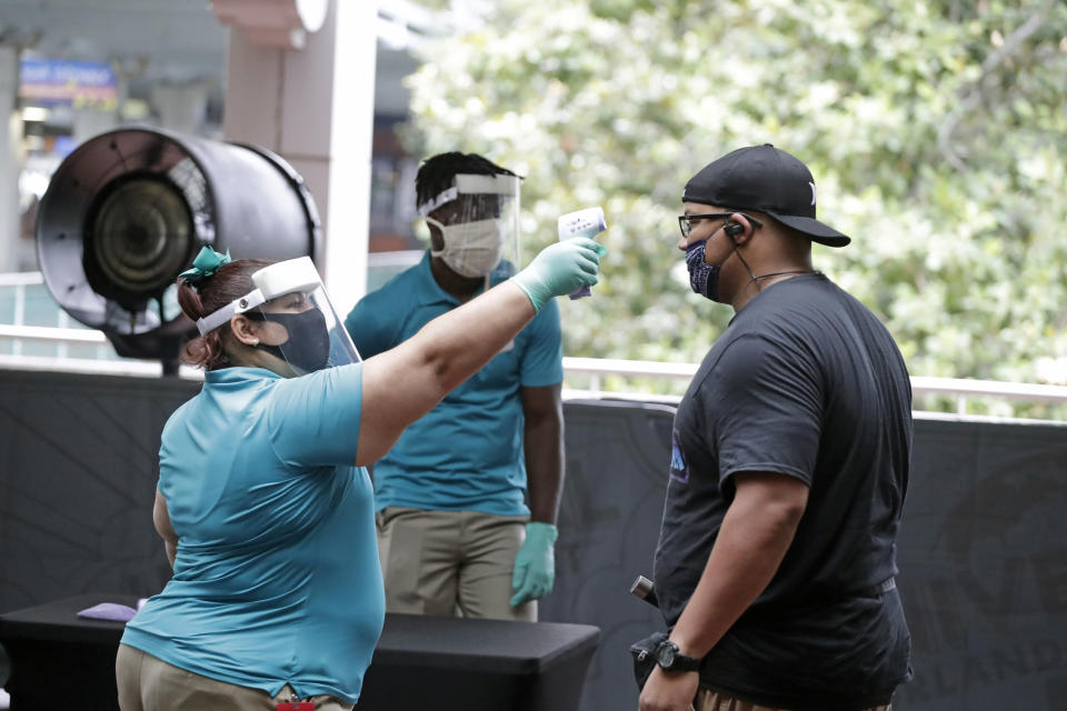 In this Wednesday, June 3, 2020 photo, a Universal Studios employee takes the temperature of a guest entering the theme park Wednesday, June 3, 2020, in Orlando, Fla. The Universal Studios theme park has reopened for season pass holders and will open to the general public on Friday, June 5. (AP Photo/John Raoux)