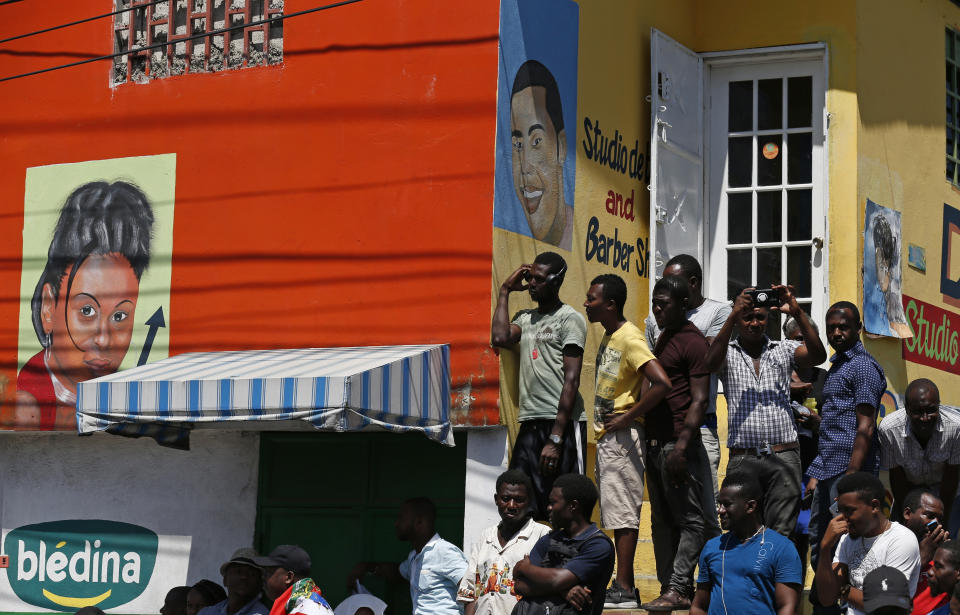 People stand on the steps of a barber shop to watch a march, led by the art community, demanding the resignation of Haitian President Jovenel Moise in Port-au-Prince, Haiti, Sunday, Oct. 13, 2019. Protests have paralyzed the country for nearly a month, shuttering businesses and schools. (AP Photo/Rebecca Blackwell)