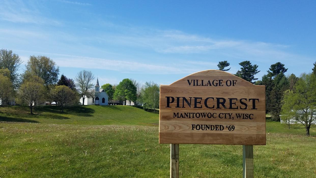 The Pinecrest sign with historic structures in the background.