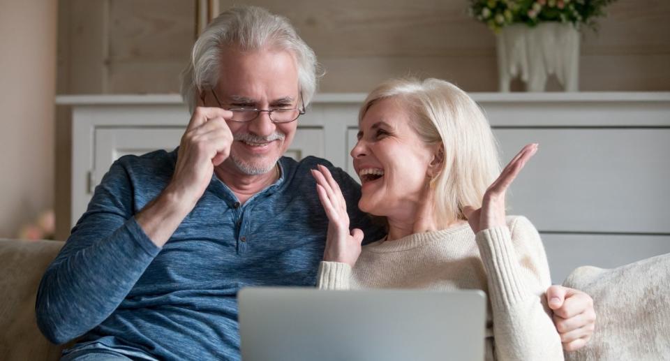 Parents celebrate lottery win on couch looking at laptop screen