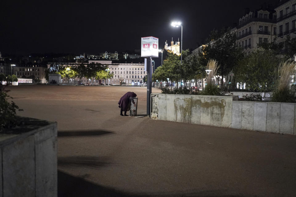 A homeless woman looks for food in the empty center of Lyon, central France, Saturday, Oct. 17, 2020. France is deploying 12,000 police officers to enforce a new curfew that came into effect Friday night for the next month to slow the virus spread, and will spend another 1 billion euros to help businesses hit by the new restrictions. (AP Photo/Laurent Cipriani)