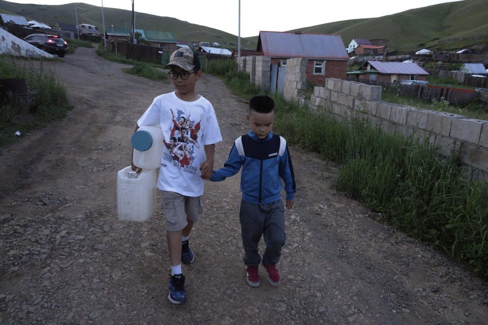 Twelve-year-old Gerelt-Od Kherlen, left, with his younger brother Gerelt-Ireedui Kherlen walks the route from a water kiosk near their home in a Ger district on the outskirts of Ulaanbaatar, Mongolia, Tuesday, July 2, 2024. Growing up in a Ger district without proper running water, Gerelt-Od fetched water from a nearby kiosk every day for his family. Carrying water and playing ball with his siblings and other children made him strong and resilient. (AP Photo/Ng Han Guan)