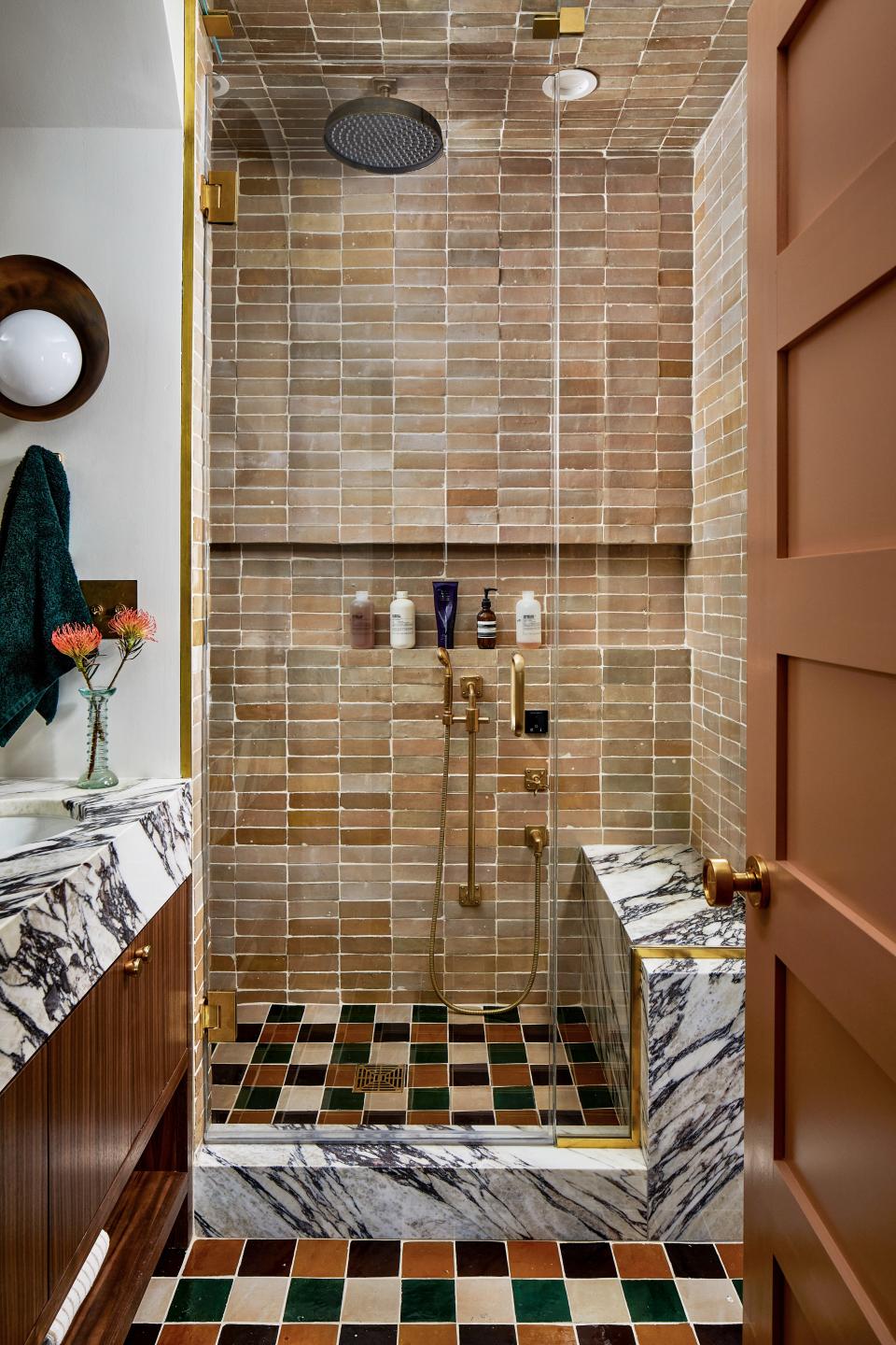 In the primary bath, Zoë dialed up the drama with outré details. One case in point? The floor, which she embellished with four-inch zellige floor tile from Clé, in the shades Golden Henna, Burnt Sugar, Cindered Olive, and Glazed Earth. She repeated the latter shade on the walls, in two-by-six tile by the same brand. “We love the palette of the tile against the marble, the elegant brass fixtures, and the luxurious steam unit. It’s a serene oasis where we can completely unwind,” says one husband. The custom walnut vanity by Fajen & Brown serves as a warm antithesis to the Calacatta Monet counter and surfaces. The wall sconce is Gallery L7’s Concha light.