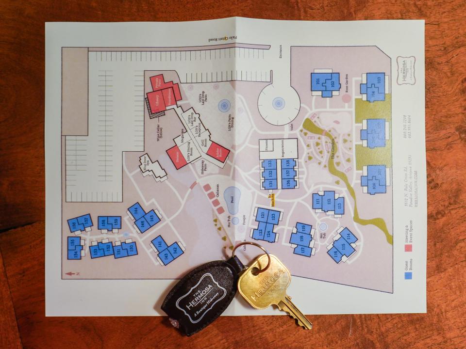 A map of a hotel with a room key on top of it on a brown, wooden table.