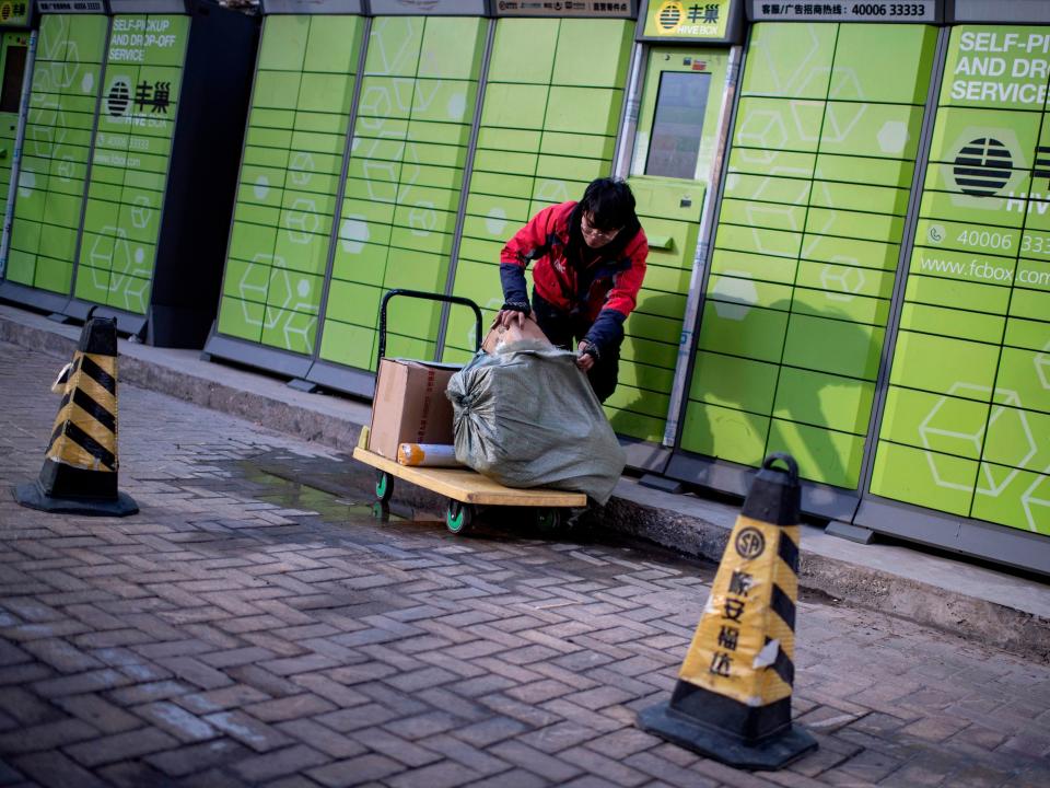 A man in a red jacket loads packages into a bright green wall of lockers in China.