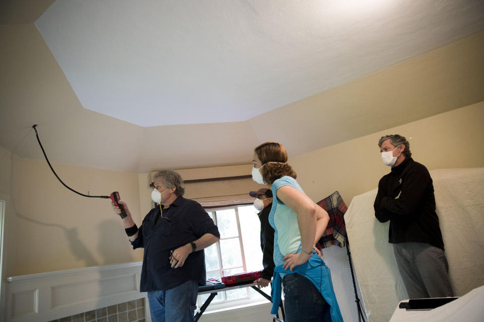 Homeowner Tom Patton, right, watches as beekeepers Sean Kennedy, left, and Erin Gleeson use a thermal camera to search for a swarm of honey bees that has gone into an attic space, Saturday, April 25, 2020, in Washington. The District of Columbia has declared beekeepers as essential workers during the coronavirus outbreak. If the swarm isn’t collected by a beekeeper, the new hive can come to settle in residential backyards, attics, crawlspaces, or other potentially ruinous areas, creating a stinging, scary nuisance. (AP Photo/Andrew Harnik)
