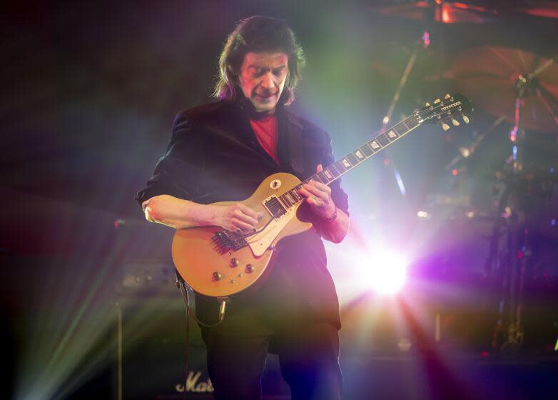 Steve Hackett plays guitar onstage with a light shining behind him