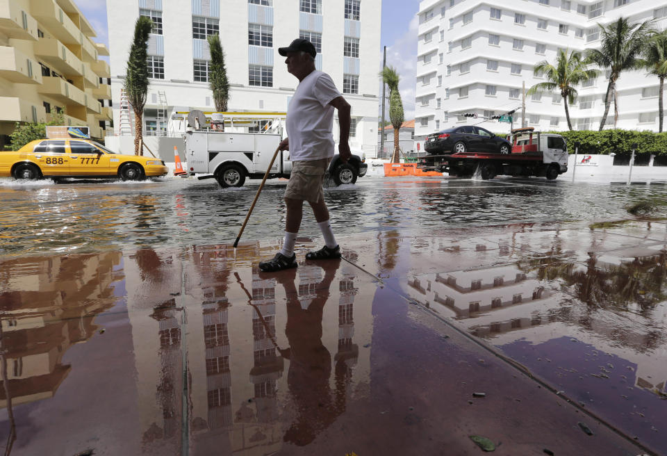 FILE- In this Sept. 30, 2015 file photo, Louis Fernandez walks along a flooded street in Miami Beach, Fla. The street flooding was in part caused by high tides due to the lunar cycle, according to the National Weather Service. When Democratic presidential candidates meet in Miami for their first debate it'll be in what you could call the country's Ground Zero for any climate-related sea level rise. (AP Photo/Lynne Sladky, File)