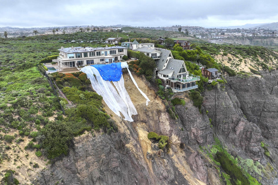 FILE - Tarps hang behind a cliff-top home above a landslide along Scenic Drive in Dana Point, Calif., on Feb. 20, 2024. California's current rainy season got off to a slow start but has rebounded with recent storms that have covered mountains in snow and unleashed downpours, flooding and mudslides. The water content of the vital Sierra Nevada snowpack has topped 80% of normal to date while downtown Los Angeles has already received more than an entire year's average annual rainfall. (Jeff Gritchen/The Orange County Register via AP)