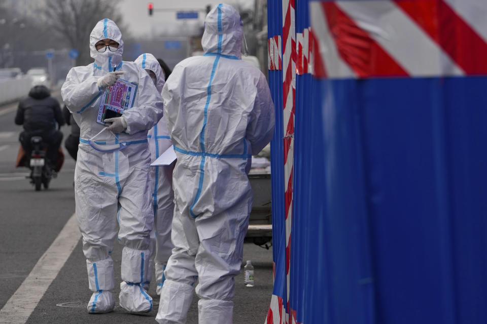 A health worker wearing a protective suit holds a map of sealed control area asks a security guard to open a doorway to a barricaded community which was locked down for health monitoring following the COVID-19 case detected in the area, Wednesday, March 23, 2022, in Beijing, China. (AP Photo/Andy Wong)