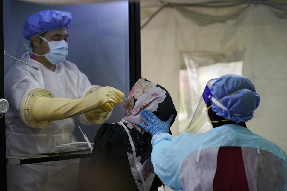 A doctor collects samples for a coronavirus test from behind a shield at a private hospital in Sunway, outside of Kuala Lumpur, Malaysia, on Wednesday, Oct. 7, 2020. The health ministry has warned that Malaysia is facing a new wave of virus cases as the outbreak has widened in recent days. New clusters have sprung up in many states amid increased travel to eastern Sabah state, a hotspot zone, for a state election last month. (AP Photo/Vincent Thian)