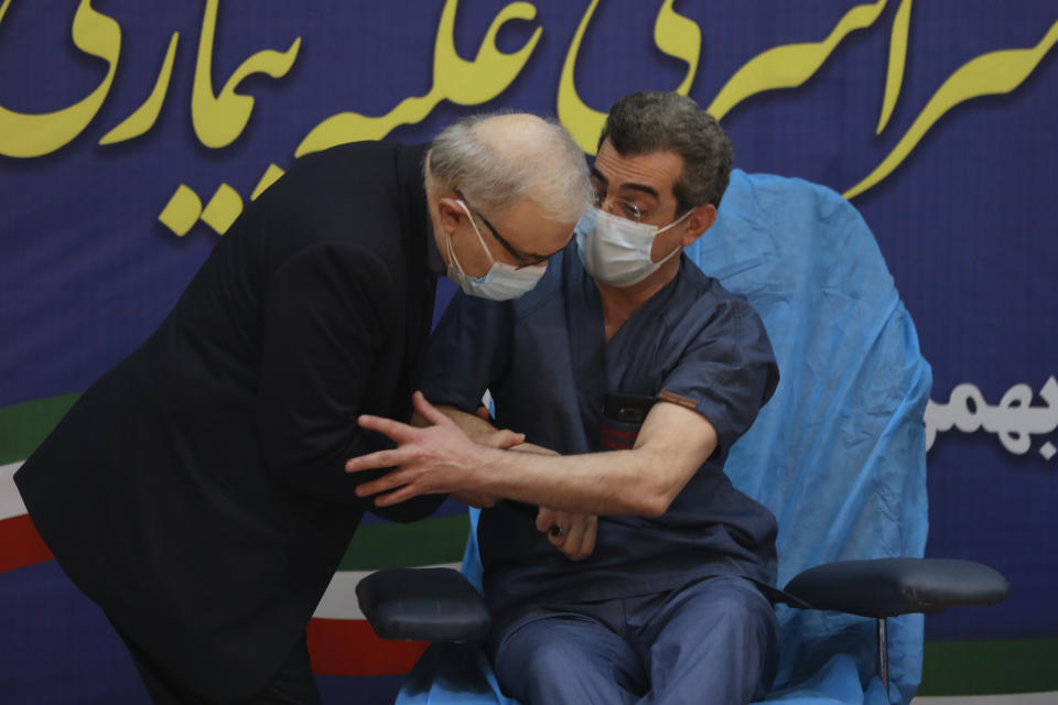 Health Minister Saeed Namaki, left, tries to the kiss hand of Dr. Fattah Ghazi as a sign of respect, after he received a Russian Sputnik V coronavirus vaccine in a staged event at Imam Khomeini Hospital in Tehran, Iran, Tuesday, Feb. 9, 2021. Iran on Tuesday launched a coronavirus inoculation campaign among healthcare professionals with recently delivered Russian Sputnik V vaccines as the country struggles to stem the worst outbreak of the pandemic in the Middle East with its death toll nearing 59,000. (AP Photo/Vahid Salemi)