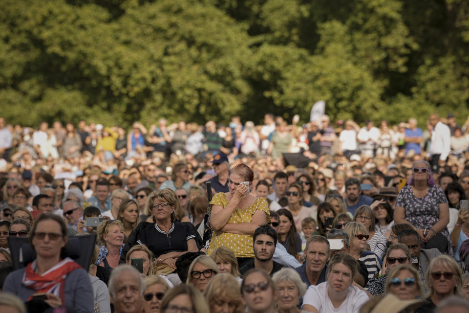 A woman wipes away tears as she joins people sitting in Hyde Park, London, Wednesday, Sept. 14, 2022 watching screens broadcasting the procession of the coffin of Queen Elizabeth II.