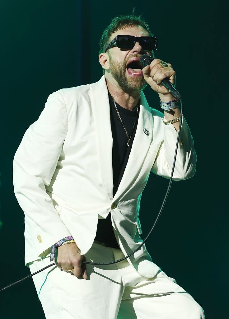 Damon in suit singing into a microphone on stage