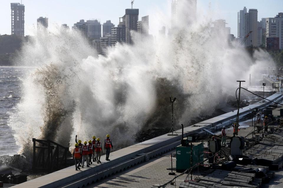 Coastal road workers walk as waves hit the city’s waterfront during high tide in the Arabian Sea at Marine Drive in Mumbai (AP)