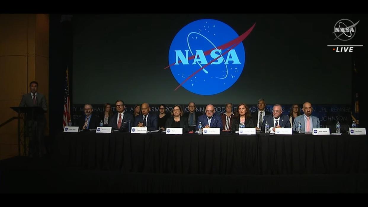  A group of people seated at a table in front of a NASA logo. 