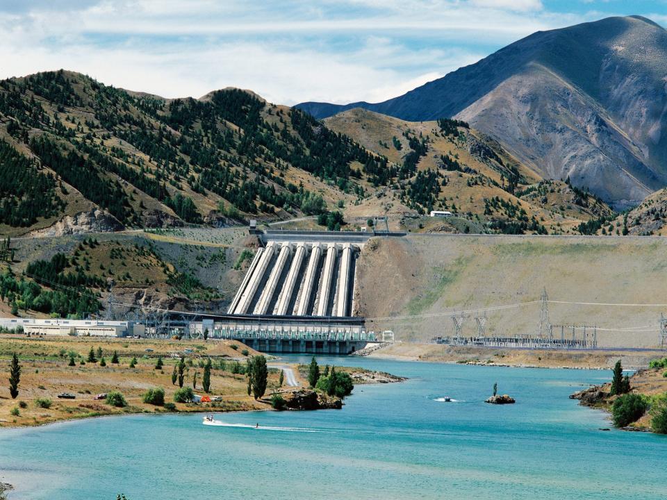 A hydroelectric plant sits in New Zealand along a mountain range and blue skies.