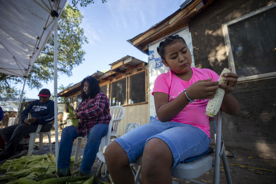 Nine-year-old Amalia Valdez, right, helps her grandmother Norma, center, peel corn at Naranjo's home in Ohkay Owingeh, formerly named San Juan Pueblo, in northern New Mexico, Sunday, Aug. 21, 2022. Friends and relatives of the Naranjos gather every year to make chicos, dried kernels used in stews and puddings. (AP Photo/Andres Leighton)