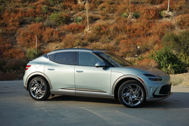 A mint green 2023 Genesis GV60 is parked in front of a hill.