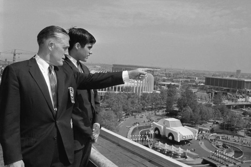 FILE - In this May 18, 1964, file photo Gov. George Romney and his son, Mitt, look out over the New York World's Fair grounds from the heliport after attending a Michigan breakfast at the Top of the Fair Restaurant. The governor and a large delegation from Michigan were there for Michigan Day at the fair. At right is part of the Chrysler exhibit and behind them is the Ford exhibit. (AP Photo, File)