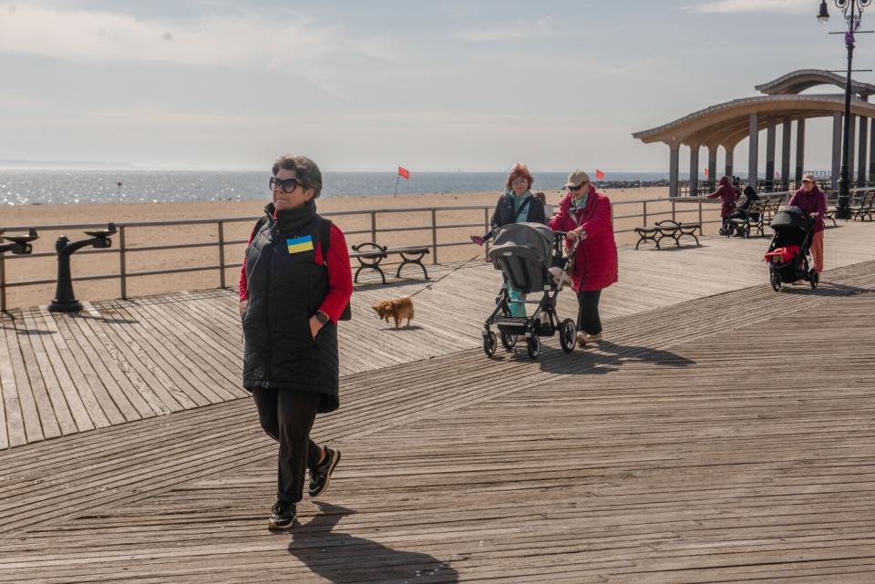 A person wearing a Ukrainian flag pin walks along the boardwalk