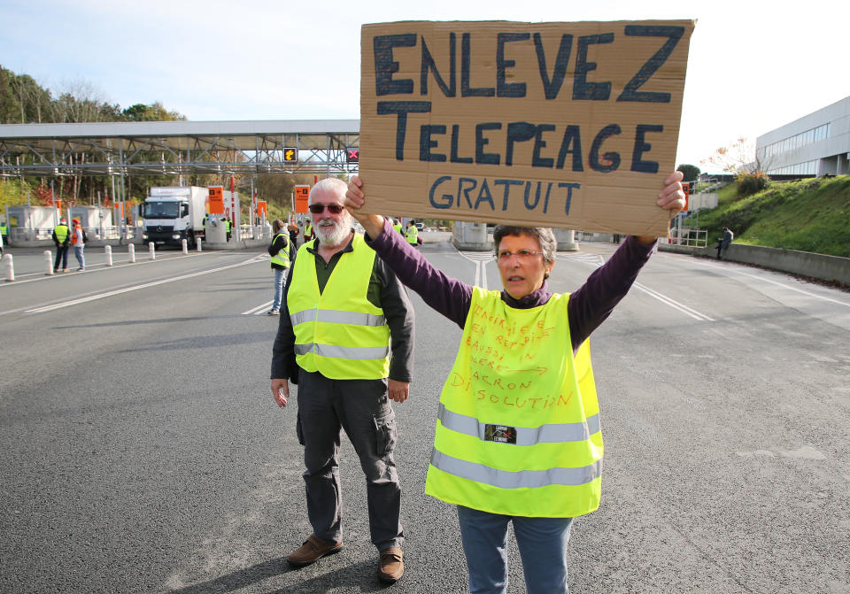 A demonstrator holds a placard reads " Free Toll" as they open the toll gates on motorway near Biarritz, southwestern France, Tuesday, Dec.4, 2018. French Prime Minister Edouard Philippe announced a suspension of fuel tax hikes Tuesday, a major U-turn in an effort to appease a protest movement that has radicalized and plunged Paris into chaos last weekend. (AP Photo/Bob Edme)