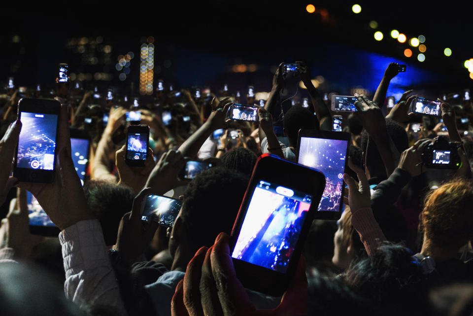A large crowd holds up smartphones to record or take photos of a stage performance at night