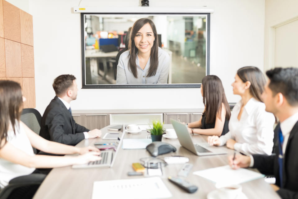 A group of business people gathered around a table looking at a screen, participating in a video conference.