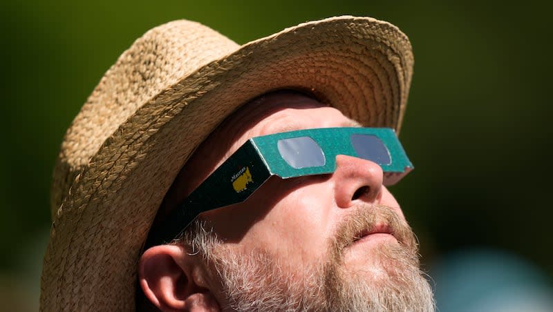 A patron looks up at the sun during a solar eclipse during a practice round in preparation for the Masters golf tournament at Augusta National Golf Club, Sunday, April 7, 2024, in Augusta, Ga.