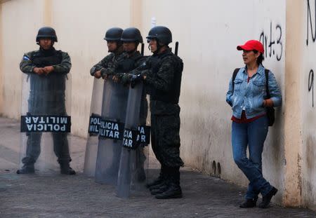 A woman is pictured next to soldiers at the main square in downtown Tegucigalpa minutes before the start time of a curfew enforced by Honduras government while the country is still mired in chaos over a contested presidential election, Honduras December 2, 2017. REUTERS/Henry Romero