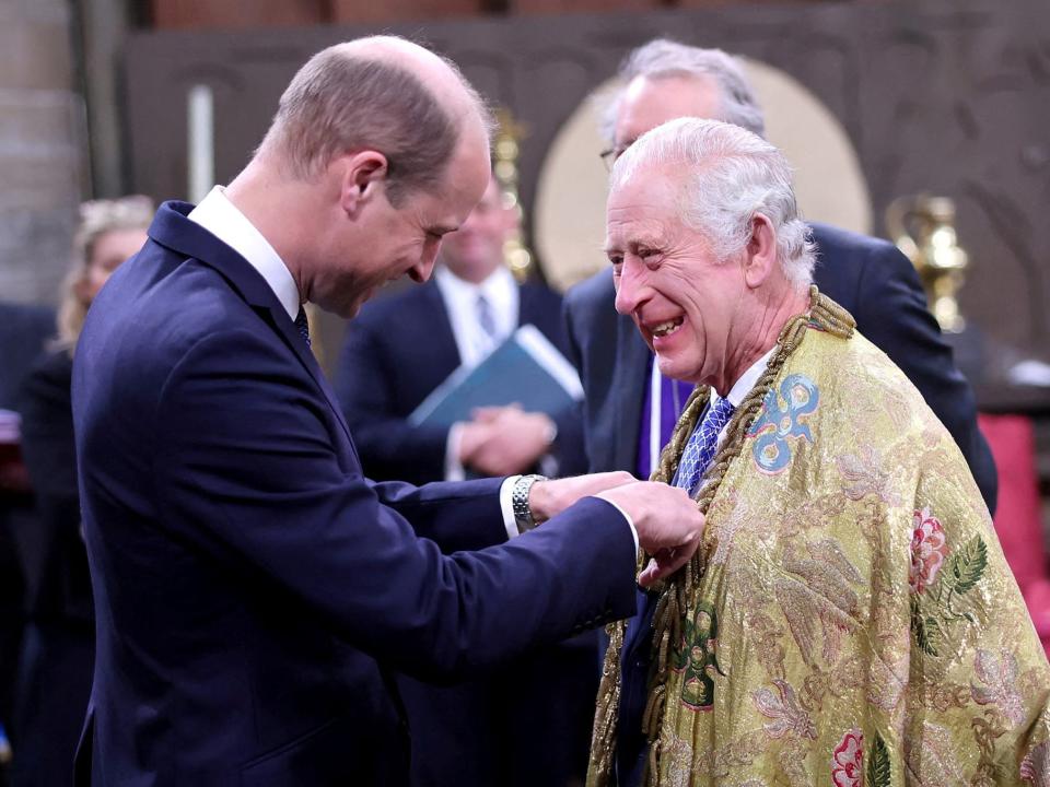 King Charles laughs as Prince William pins something to his chest.