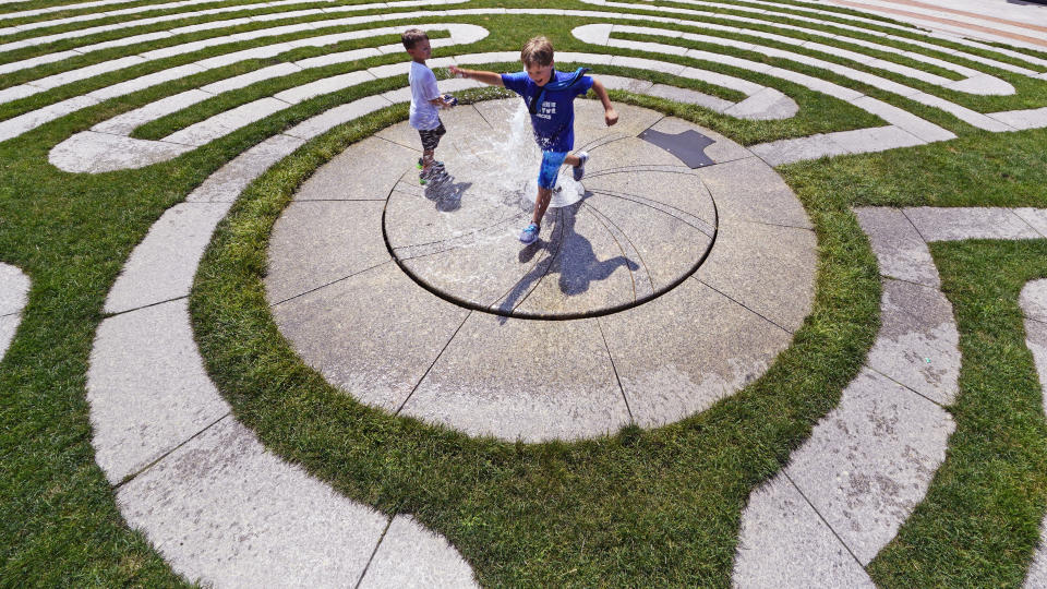 Dylan Schoenfeld, 9, of California, leaps over a fountain while cooling off with his brother Charlie, 5, while on vacation during a summer heat wave, Thursday, July 21, 2022, in Boston. Dangerously high temperatures Thursday threatened much of the Northeast and Deep South as millions of Americans sought comfort from air-conditioners, fire hydrants, fountains and cooling centers. (AP Photo/Charles Krupa)