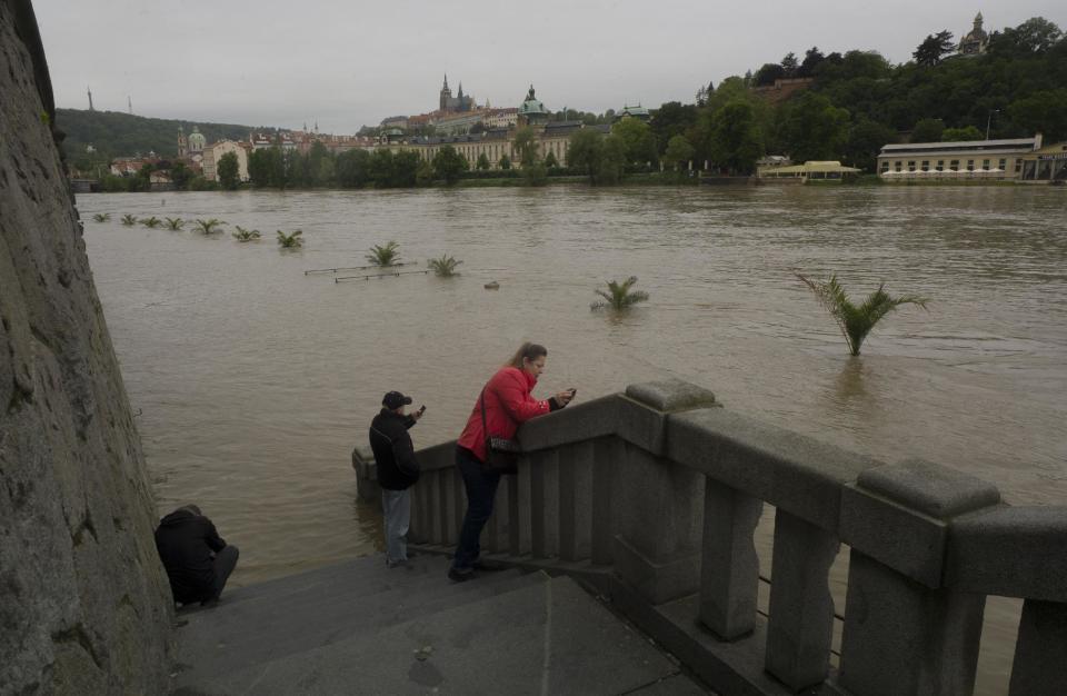 Varias personas sacan fotos de las copas de los árboles emergiendo de las aguas desbordadas del río Vltava, en Praga.