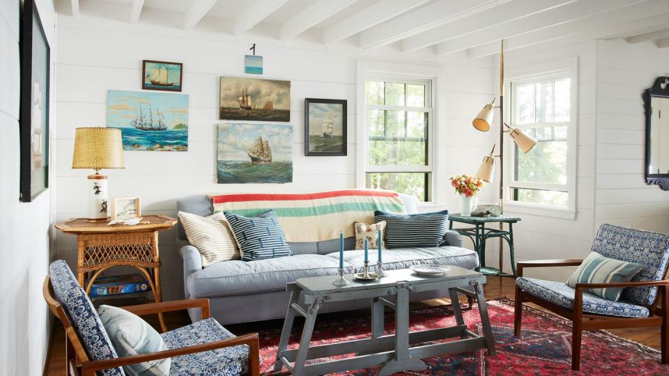 art gallery wall of ship paintings casually arranged on white shiplap wall in john wentworth and jamie gluck's 1940s cedar cottage in madison, maine