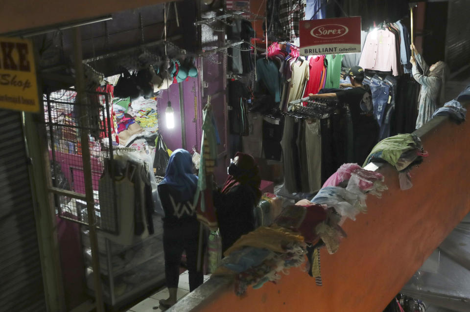 Clothes sellers prepare to open their shops at a quiet market in Jakarta, Indonesia, Friday, April 10, 2020. Authorities began stricter measures to halt the new coronavirus' spread in Indonesia's capital Friday, with its normally congested streets empty after death toll spiked in the past week. (AP Photo/Achmad Ibrahim)