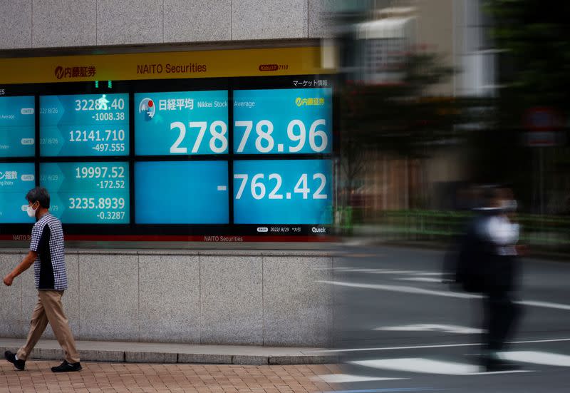 A man wearing a protective mask amid the coronavirus disease (COVID-19) outbreak, walks past an electronic board displaying Japan's Nikkei index outside a brokerage in Tokyo