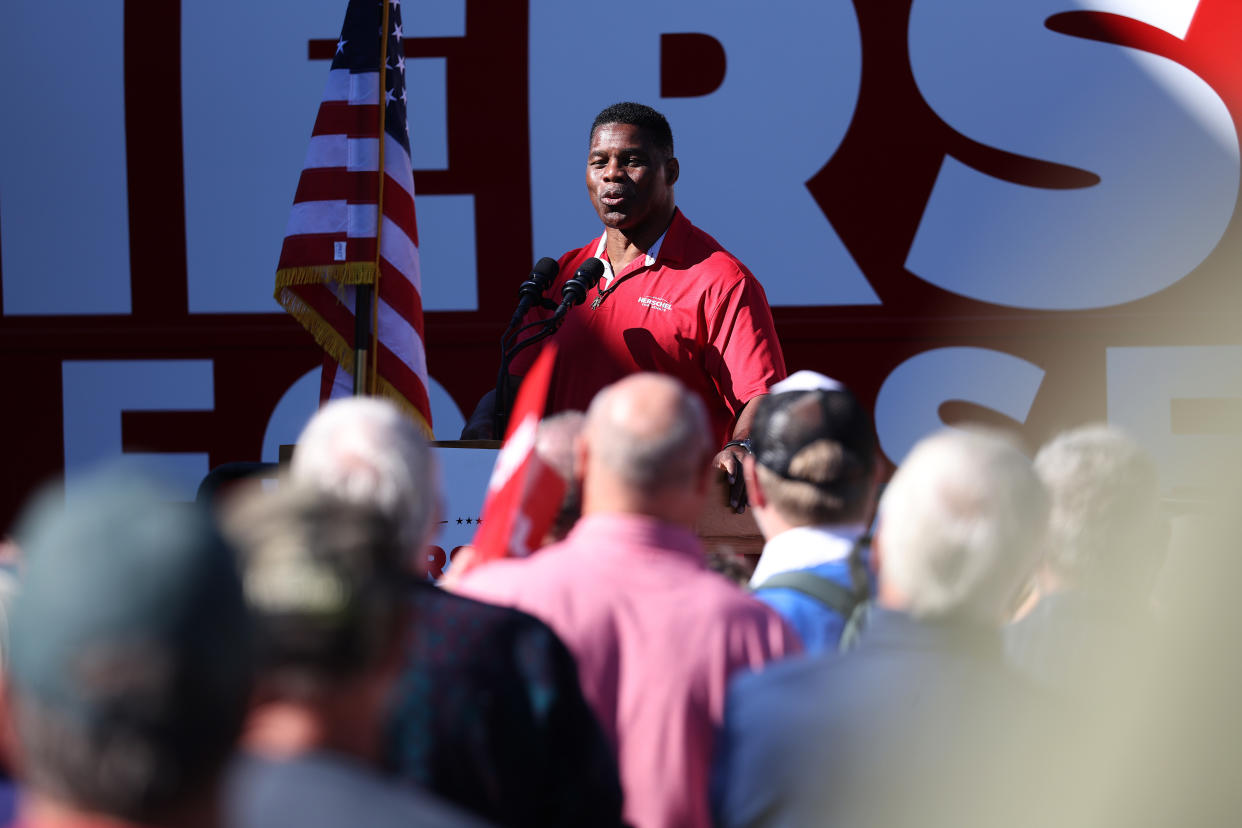 Herschel Walker speaks into two microphones at a podium before a crowd of people.