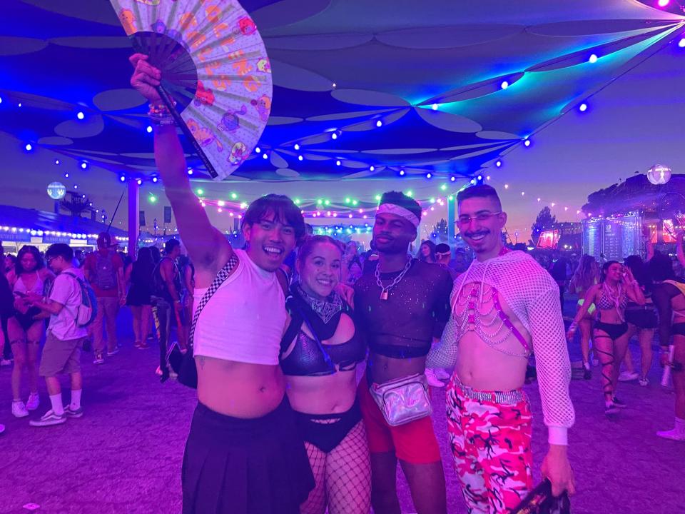 Four people pose at a music festival in pink and blue lighting