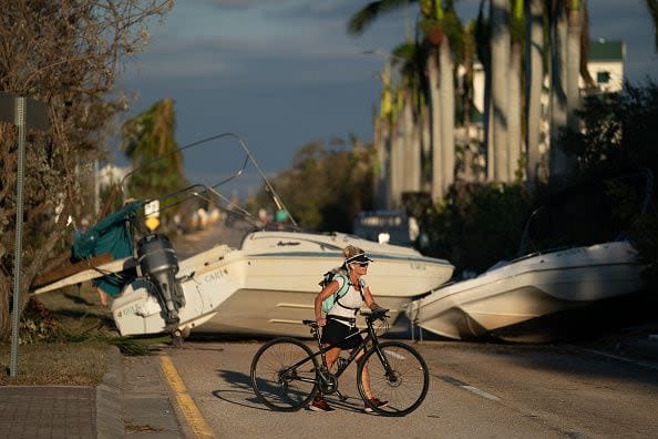 A woman walks her bike past boats blocking a road after Hurricane Ian on September 29, 2022, in Bonita Springs, Florida.