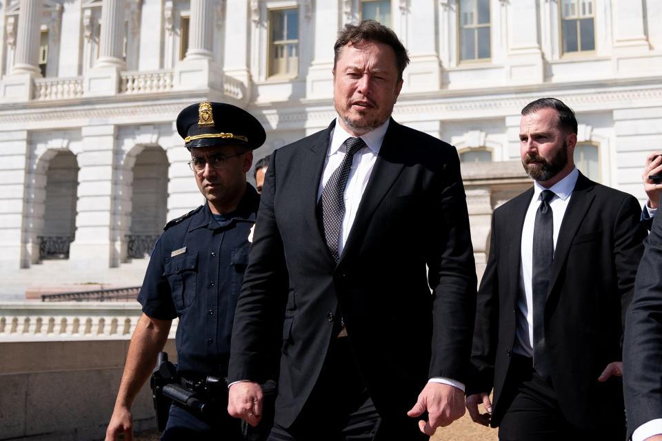 Elon Musk, wearing a black suit and tie and flanked by a police officer and a body guard, departs following a meeting at the US Capitol in Washington, DC, on September 13, 2023