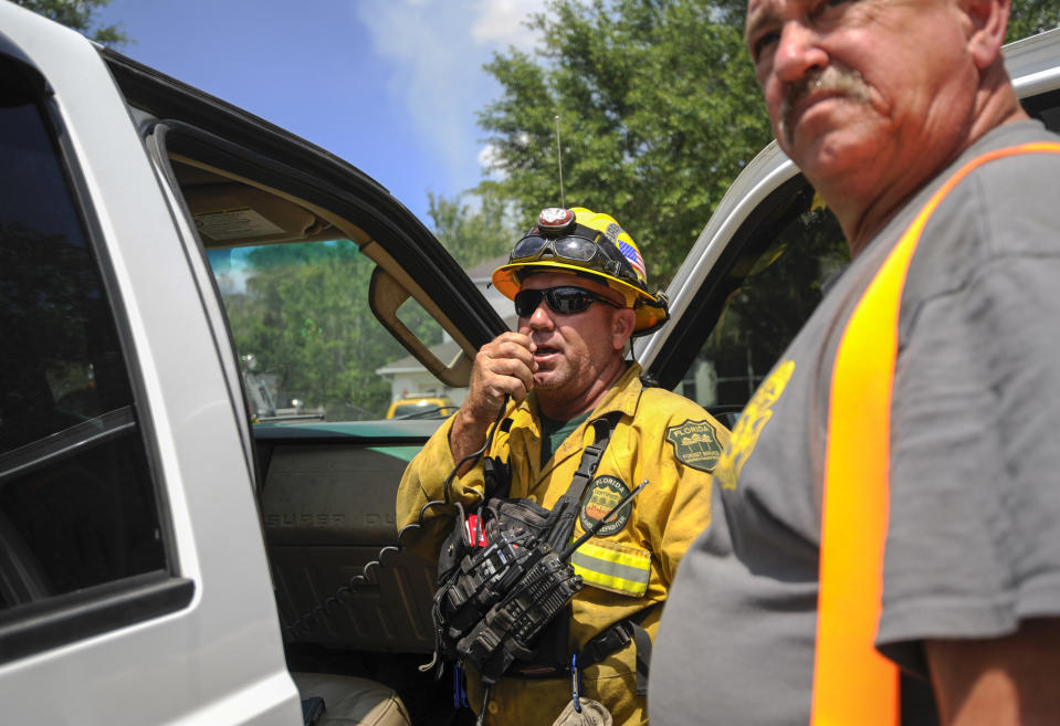John DeWolfe, with Florida Forest Service, center, speaks on a two-way radio as a Pasco County firefighter who asked not to be identified, looks on Tuesday, April 11, 2017 in Land O' Lakes, Fla. The Silver Palms Fire burned close to homes in the Suncoast Lakes subdivision Tuesday, forcing residents to use garden hoses on vegetation and roofs around their property. (Chris Urso/The Tampa Bay Times via AP)